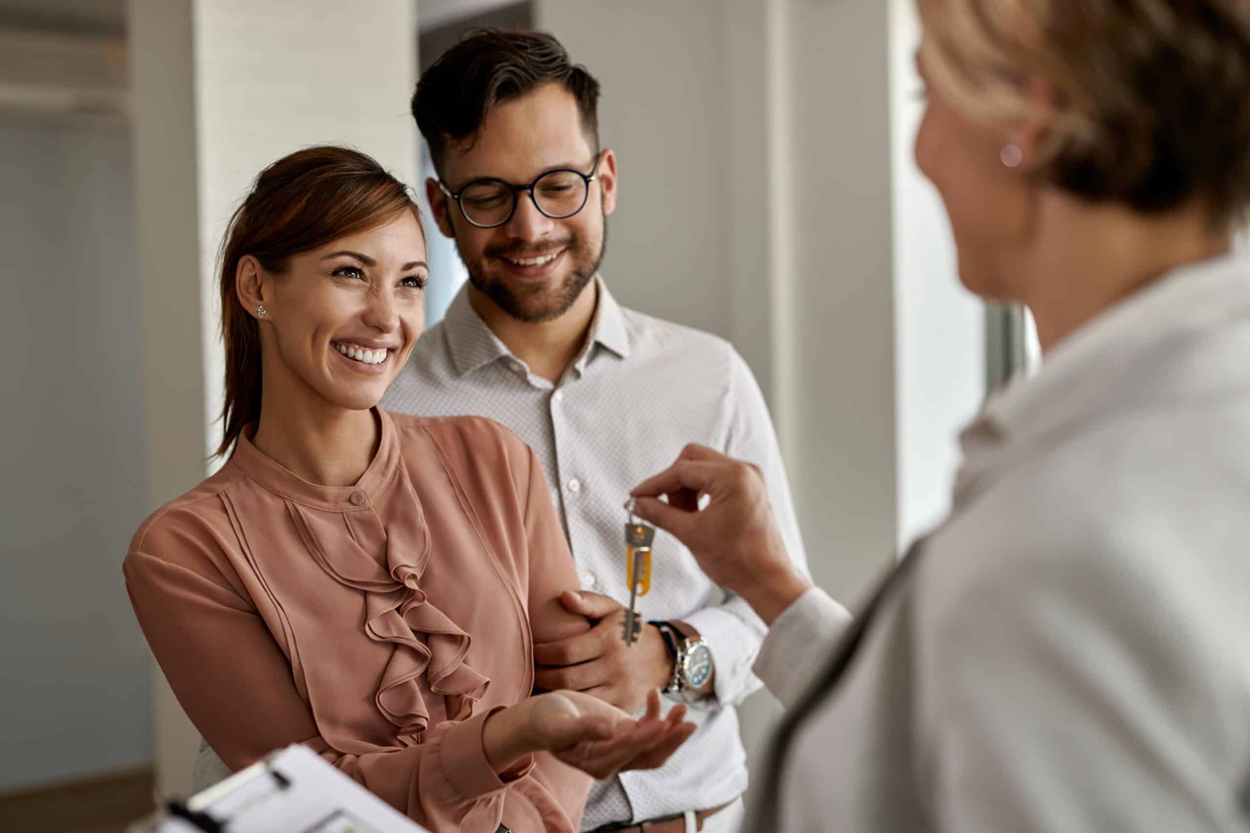 Happy couple receiving house keys from agent representing Texas Homebuyers purchasing a new home in the Texas market.