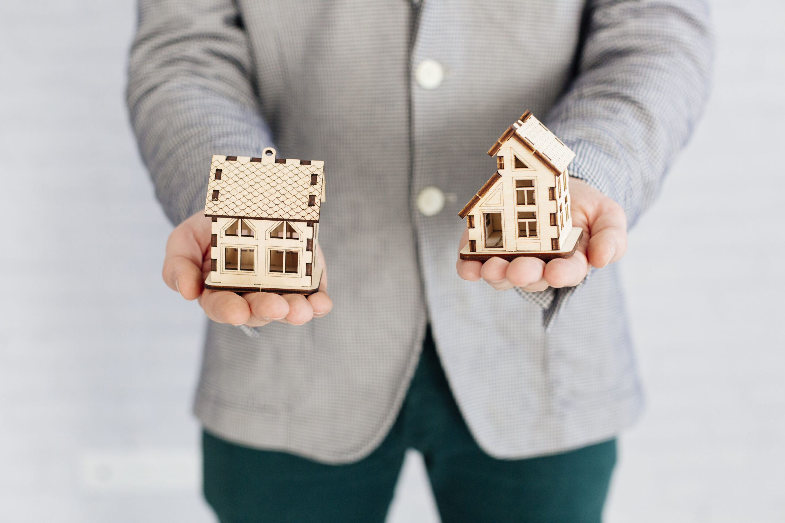 Professional holding two miniature house models, illustrating a comparison between FHA loans and Non-QM loan options for homebuyers with different financing needs.